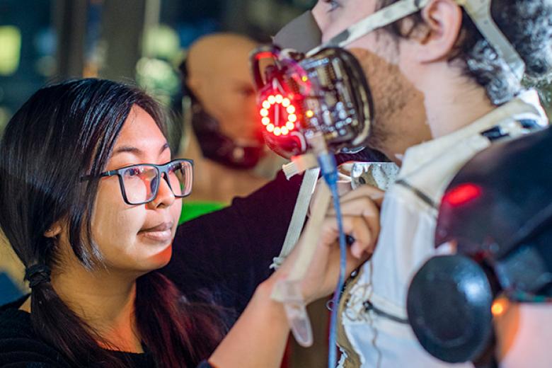 A female student adjust the robotic-like costume modeled by a male student.